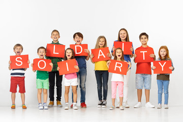 Wall Mural - Solidarity of sweet hearts. Group of happy screaming children, young team or teenagers with a red banners isolated in white studio background. Education and advertising concept