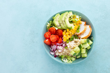 Lunch bowls with grilled cgicken meat, rice and fresh salad of avocado, cucumbers, corn, tomato and onion