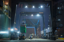 Operation Of Container Terminal At Night. Unloading Container Ship At Night. Mooring Cranes Unload Container Ship At Night