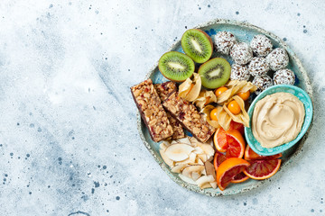 Poster - Healthy vegan dessert snacks - protein granola bars, homemade raw energy balls, cashew butter, toasted coconut chips, cape gooseberry, kiwi, blood orange. Concept of healthy sweets for children.