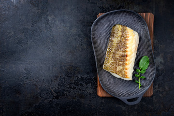 Fried Japanese skrei cod fish filet with wasabi lettuce as top view on a modern design plate with copy space left