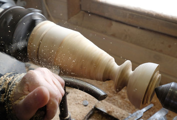 Мan grinds a wooden candlestick on a lathe