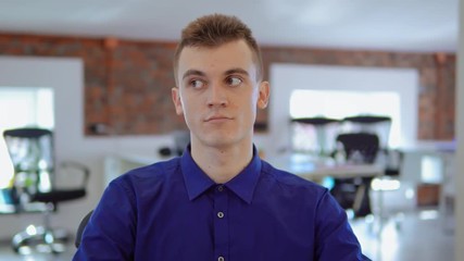 Poster - employee shifts eyes from left to right then looking at the camera. portrait young caucasian man wearing casual blue shirt sitting at the workplace in modern office.