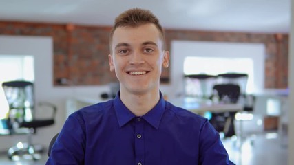 Poster - cheerful employee laughing looking at the camera front view. portrait young caucasian wearing casual blue shirt man sitting at the workplace in modern office.