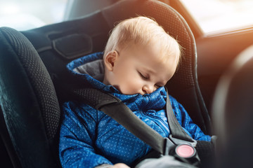 Cute caucasian toddler boy sleeping in child safety seat in car during road trip. Adorable baby dreaming asleep in comfortable chair during journey in vehicle. Children care and safety on roads