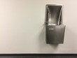 Shiny metal drinking fountain on white wall