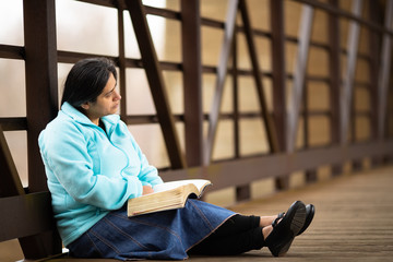 Wall Mural - Hispanic Woman Sitting On A Bridge And Reading Bible
