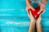 Close-up portrait of lovely couples hands holding soft red heart shape on wooden background. Relationship  of new generation with eldery people concept - Image