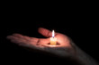 © metelevan - paraffin candle memory lit on the palm of a man, the background is dark