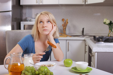 woman eating healthy food in the kitchen at the table. disappointment in healthy eating tired to eat right, tired of dieting. choice of proper or improper nutrition.  the girl is obsessed with diets.