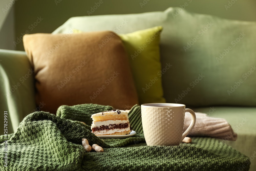 Cup of hot tea with tasty cake on sofa