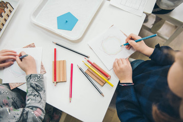 Montessori Education. Montessori School. Learning materials in a montessori methodology school. Geometric materials. Color pencils. Little girls drawing on paper.