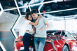 © LIGHTFIELD STUDIOS - happy curly woman hugging handsome man while standing near automobile