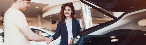Cuadros en Lienzo panoramic shot of smiling car dealer and customer shaking hands in car showroom