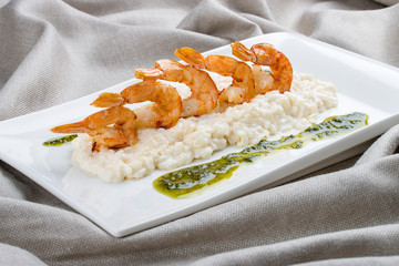 Wall Mural - Shrimps with risotto and pesto on a white plate, on a textile background