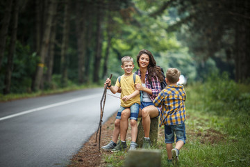 Wall Mural - mother and her little sons hiking . they're taking a break and sitting on a rock by the road.