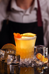 Wall Mural - Whiskey Sour alcohol cocktail with orange slice and ice cubes on black mirror background made by man bartender