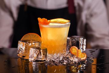 Wall Mural - Whiskey Sour alcohol cocktail with orange slice and ice cubes on black mirror background made by man bartender