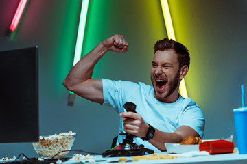 Wall Mural - handsome cyber sportsman playing video game with joystick and showing yes gesture