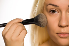 Young blonde applying powder foundation with brush on white background
