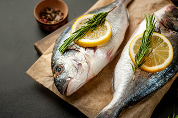 two fresh raw dorado fish on a cutting board with spices and olive oil on a stone background