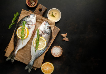 two fresh raw Dorado fish on a cutting board with spices and olive oil on a stone background. Space for text