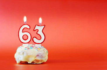 Sixty three years birthday. Cupcake with white burning candle in the form of number 63. Vivid red background with copy space