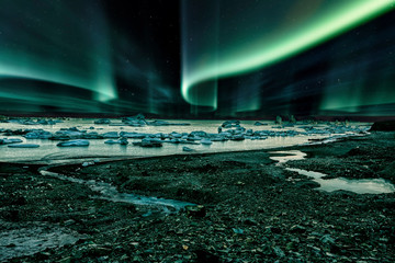 iceberg floating in greenland fjord at night with green northern lights