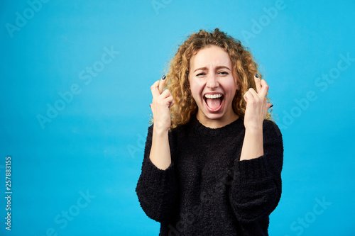 Fotografía Emotional satisfied young attractive redhead curly woman with opened mouth crossing fingers for good luck