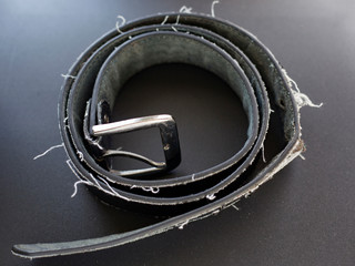 ripped leather belt with protruding threads on a dark background