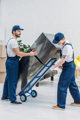 Canvas Print - two movers using hand truck while transporting refrigerator in apartment