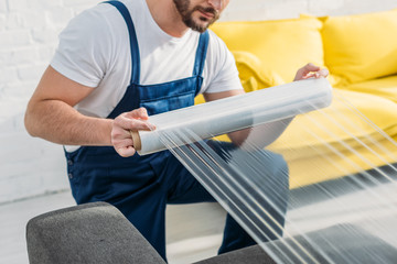 Wall Mural - cropped view of mover wrapping furniture with roll of stretch film in apartment