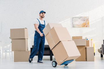 mover in uniform transporting  cardboard boxes on hand truck in apartment