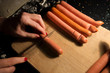 © lainen - Preparing tanned wiener sausages in pizza dough. Cutting sausages on wooden board before baking. Dark background in kitchen. Making snacks for family and friends