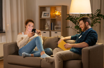 leisure and people concept - happy couple with smartphone and book at home in evening