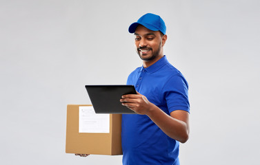 mail service, technology and shipment concept - happy indian delivery man with parcel box and tablet computer in blue uniform over grey background