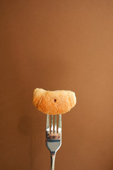 Poster - Croissant on a fork. Brown background with empty place for text