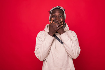 Wall Mural - Young cool black man covering his mouth isolated on red background