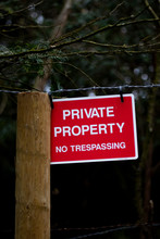Private Property No Trespassing Sign Fixed To Barbed Wire Fence Protecting Woodland With Shallow Depth Of Field