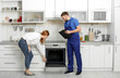 Housewife with repairman near modern oven in kitchen