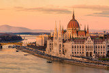 Fototapeta Miasto - Cityscape of Budapest with bright parliament illuminated by last sunshine before sundown and Danube river with bridge. Pink and purple colors of sky reflecting in water during sunset.