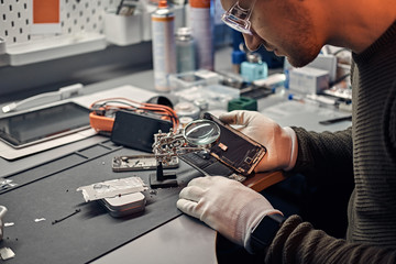 Wall Mural - The technician uses a magnifying glass to carefully inspect the internal parts of the smartphone in a modern repair shop