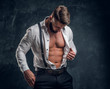 © Fxquadro - A stylish young man with a muscular body in the unbuttoned white shirt with suspenders. Studio photo against a dark wall background