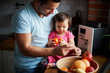 © Westend61 - Father and baby girl eating fruit in kitchen at home
