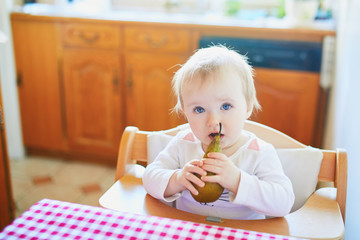 Wall Mural - Cute baby girl eating pear in the kitchen