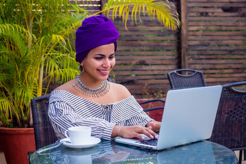 Smiling beautiful indian girl with ethnic turban on head culture working on laptop outdoors summer cafe