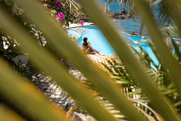 Wall Mural - Young woman with coconut relaxing at the swimming pool in summer time. Vacation on Bali island, Indonesia.