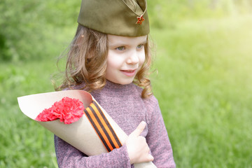 Wall Mural - Girl child in a military cap holds a bouquet of red carnations on the victory day holiday on May 9. St. George ribbon - the symbol of the great Victory/Victory Day.