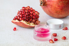 A Small Jar With A Gel For Face Skin Care And A Pieces Of Ripe Red Pomegranate On A Light Background. Selective Focus.