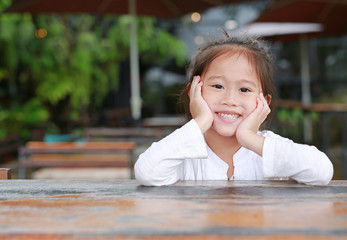 Happy little Asian kid girl lying on the wooden table with looking camera.